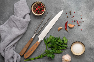 Cooking background, knife, meat fork, spices and greens. Gray concrete background. Top view, flat lay