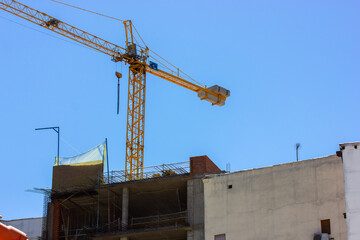 A yellow construction crane at a construction site against a blue sky. Construction business, real estate, construction of modern high-rise buildings. Real estate engineering.