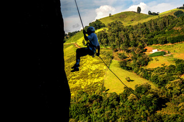 Pessoa escalando montanha com paisagem rural ao fundo