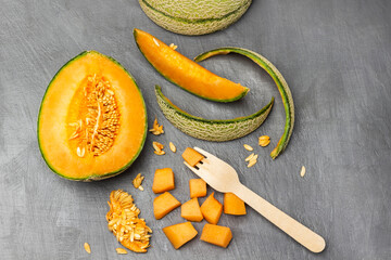 Half a melon. Peel, pieces of melon and a wooden fork. Seeds on the table.