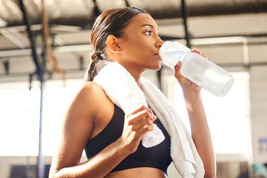 Relax, fitness or Indian woman drinking water in gym after training, workout or exercise to hydrate her body. Fatigue, wellness or tired girl with bottle for healthy liquid hydration on resting break