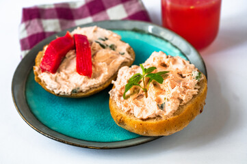 2 canapés with salmon spread and fresh cheese on blue plate, glass of juice, cloth.