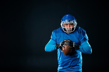 Portrait of a man in a blue uniform for american football on a black background. 
