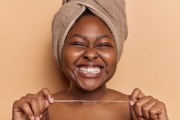 Dental flossing concept. Cheerful dark skinned woman holds dental floss shows white perfect teeth...