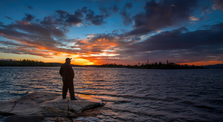 Sunset in Karelia. Nature Russia. Man admires sunset. Guy on seashore. Traveler with back to camera. Karelia on summer evening. Man stands on stone coast. Landscape Russia. Sunset over Karelia nature