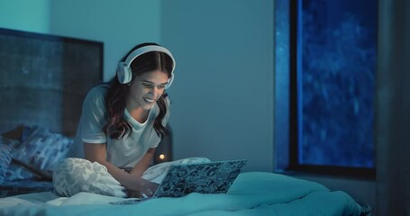 Happy Indian excited freelancer girl enjoy video work on laptop late night at home. Young beautiful smile female use headphones sitting on bed get new distant job opportunity celebrates online success
