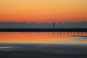 Pf&auml;hle spiegeln sich im Wasser bei Sonnenuntergang