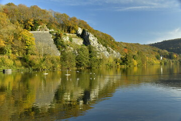 Fototapeta na wymiar Pans de rochers couverts de végétation en automne se reflétant dans la Meuse à Profondeville 