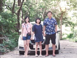 Cheerful asian family  father, mother and daughter standing near car, enjoy journey together outdoor in summer. Family trip, vacation and travel at auto