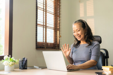 An old businesswoman in her sixties sitting at a table using a laptop. middle aged woman working at home Meet and chat online using the internet on social media.