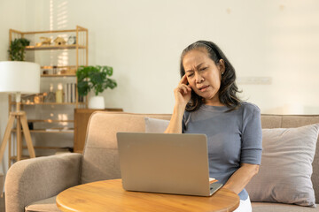 Elderly woman, health problems, vision and people. Close up of asian old woman sitting on sofa and having headache at home from working in front of laptop.