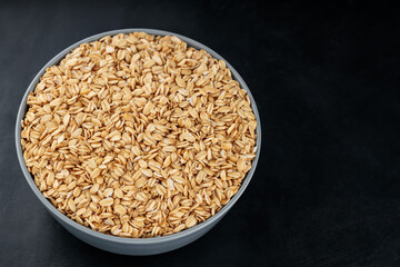 Oat flakes in a bowl on a dark background. Uncooked rolled oats for a healthy diet. Gluten free diet concept. Copy space