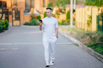 Stylish man in white costume looking at mobile phone walking at the street