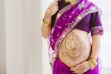 Pregnant woman in purple sari. mehendi. Indian painting on woman's hands and pregnant belly with...