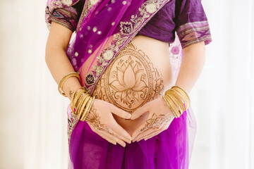 Pregnant woman in purple sari. mehendi. Indian painting on woman's hands and pregnant belly with henna tattoo on white room background