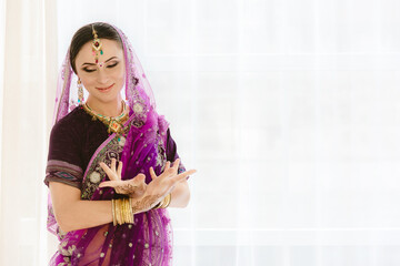 Pregnant woman in purple sari. mehendi. Indian painting on woman's hands and pregnant belly with henna tattoo on white room background