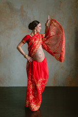 Pregnant woman in red sari. mehendi. Indian painting on woman's hands and pregnant belly with henna tattoo on room background