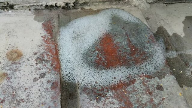 Agua con jab&oacute;n  form&aacute;ndose con abundante espuma  en el piso de cemento.