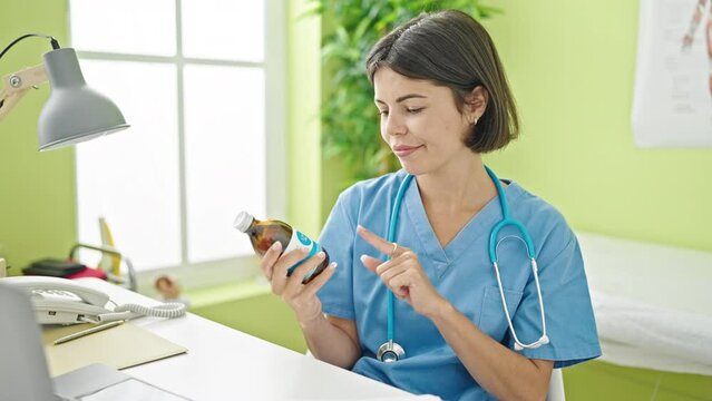 Young beautiful hispanic woman doctor smiling confident holding medication bottle at clinic
