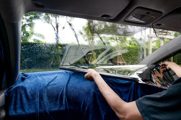 Car side window film removal and tinting installation. Male auto specialist worker tinting car window film on front windscreen glass surface.