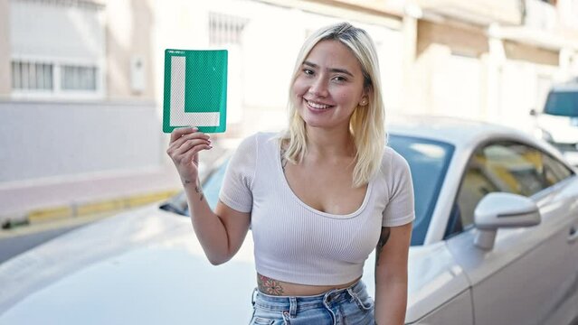 Young beautiful hispanic woman holding new drive license standing by car at street