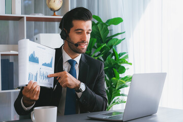 Business man wearing headphone present financial data or BI paper via laptop during online meeting....
