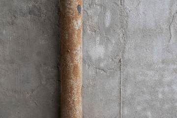 Old rusty metal water pipe against a shabby concrete wall