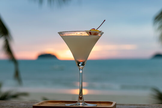 Cocktail glass decorated with a slice of lime and cherry on the background of the sea and sunset. Refreshing cocktail Margarita.