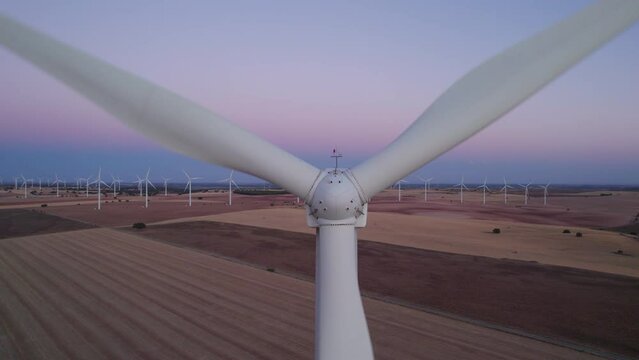 Aerial top view of a Close-up to a Windmill (zoom out) in Wind turbines Farm at sunset. Numerous windmills rotating in the background. Cuenca, Castilla La Mancha, Spain