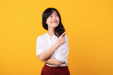 Obraz premium Portrait young asian woman enterpriser happy smile dressed in white shirt and red plants showing pointing finger hand gesture to free space isolated on yellow studio background. Attention to product