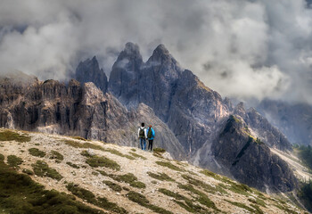 Fototapeta na wymiar Couple of travelers with backpacks hold hands standing over a cliff and looking at the beautiful mountains landscape. Travel and tourism concept