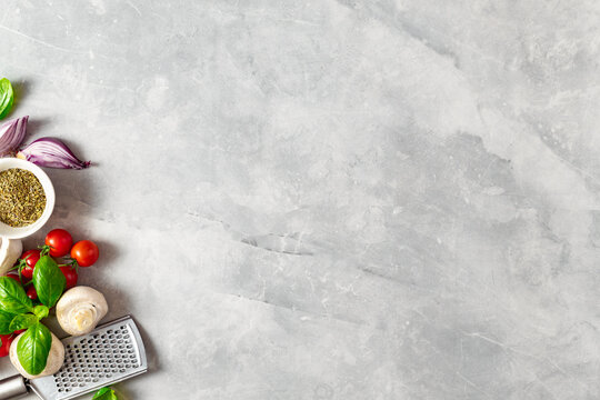 Food cooking ingredients background with fresh vegetables, herbs, spices and olive oil on white stone table top view. Healthy vegetarian eating