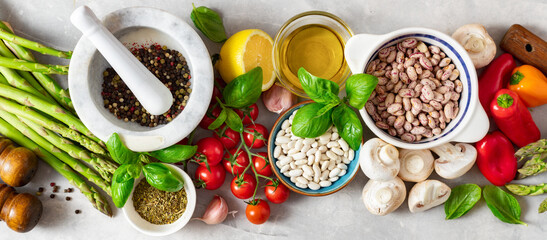 Food cooking ingredients background with fresh vegetables, herbs, beans, spices and olive oil on white stone table top view. Healthy vegetarian eating
