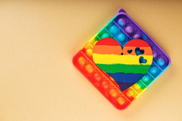 Fototapeta na wymiar Multicolored pop it fidget toys and rainbow heart on beige background. LGBT equal rights movement and gender equality concept. Top view. Copy space