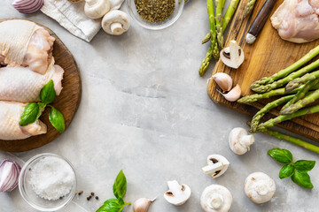 Frame of fresh pieces of chicken thigh meat on wooden cutting board with ingredients for cooking healthy food on light background top view