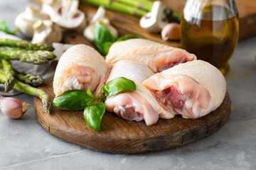Fresh pieces of chicken thigh meat on wooden cutting board with ingredients for cooking healthy food