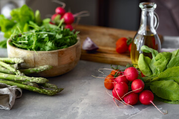 Raw set ingredients for cooking healthy vegetarian food. Bowl of arugula, branches of cherry tomatoes, radishes, asparagus and olive oil