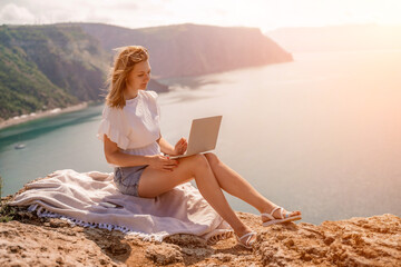 Freelance woman working on a laptop by the sea, typing away on the keyboard while enjoying the beautiful view, highlighting the idea of remote work.