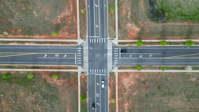 Cars at intersection of road with stoplights driving through from aerial drone top down 4K 