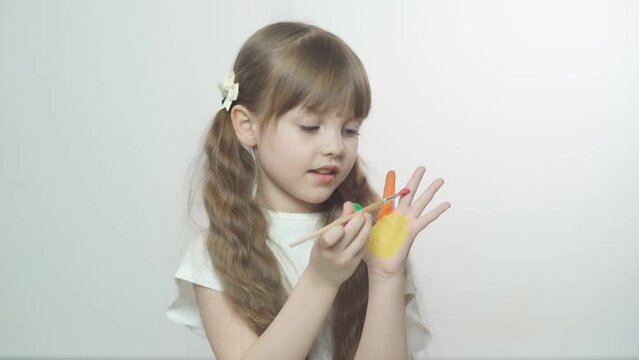 A little preschool girl with brown hair paints palms of different colors. Sensory development and experiences, themed activities with children, fine motor skills development.