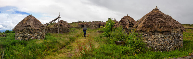 Panoramic landscape of Castromao, in Orense, with a person walking in the middle of huts with thatched roofs, surrounded by green nature, summer of 2021, Spain.