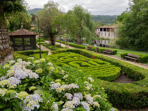 Paisaje de un laberinto de setos verdes en primer plano y &aacute;rboles y monta&ntilde;as al fondo con cielo nuboso, en el pueblo de Allaritz, Orense, verano de 2021.