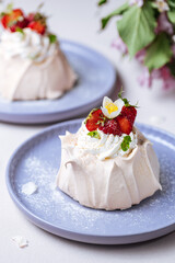 Two small pavlova cakes from meringue decorated with fresh strawberries on a pink plate. Bright scene with flowers as decoration.