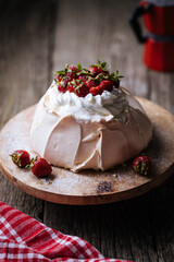 Pavlova cake decorated with strawberries in rustic, wooden atmosphere. Cake is made from meringue and whipped cream