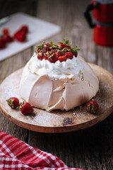 Pavlova cake decorated with strawberries in rustic, wooden atmosphere. Cake is made from meringue and whipped cream