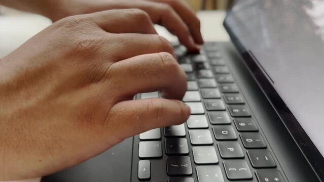 Manos de hombre escribiendo en un teclado color negro de iPad Pro. Trabajando en oficina o en casa. 