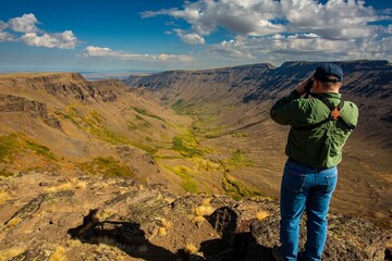 Steens Mountains, Oregon - 9/20/2018:  A man, looking east through binoculars, standing at the top of Keiger gorge in the steens mountains, near Frenchglen, Oregon.