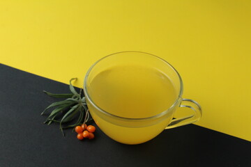 sea buckthorn tea drink on a black yellow bright background. Sea buckthorn drink tea juice in a glass cup next to a spout of sea buckthorn leaves orange berries on a black and yellow background