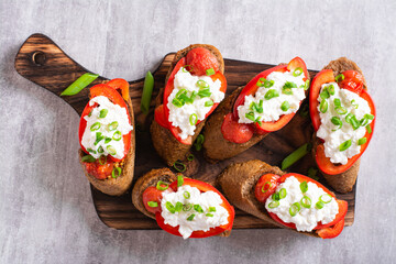 Close up of crostini with baked tomatoes, bell peppers, ricotta and herbs on a wooden board top view