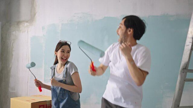 New home,Repair,happy,New life,insurance,carefree relationship,love lifestyle,renovation and decorating concept.Happy Young asian couple dancing making funny moves and painting walls at new apartment